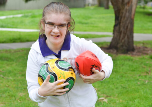 young girl at a park holding soccer and afl football
