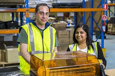 A packing supported employee stands at a shrink wrap machine next to his support worker