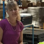 warehouse supported employment worker gail in warehouse with boxes behind her