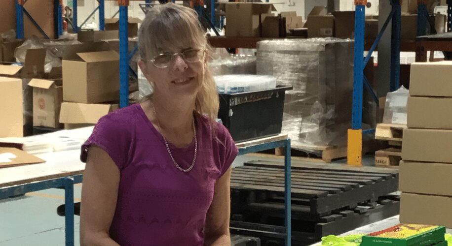 warehouse supported employment worker gail in warehouse with boxes behind her