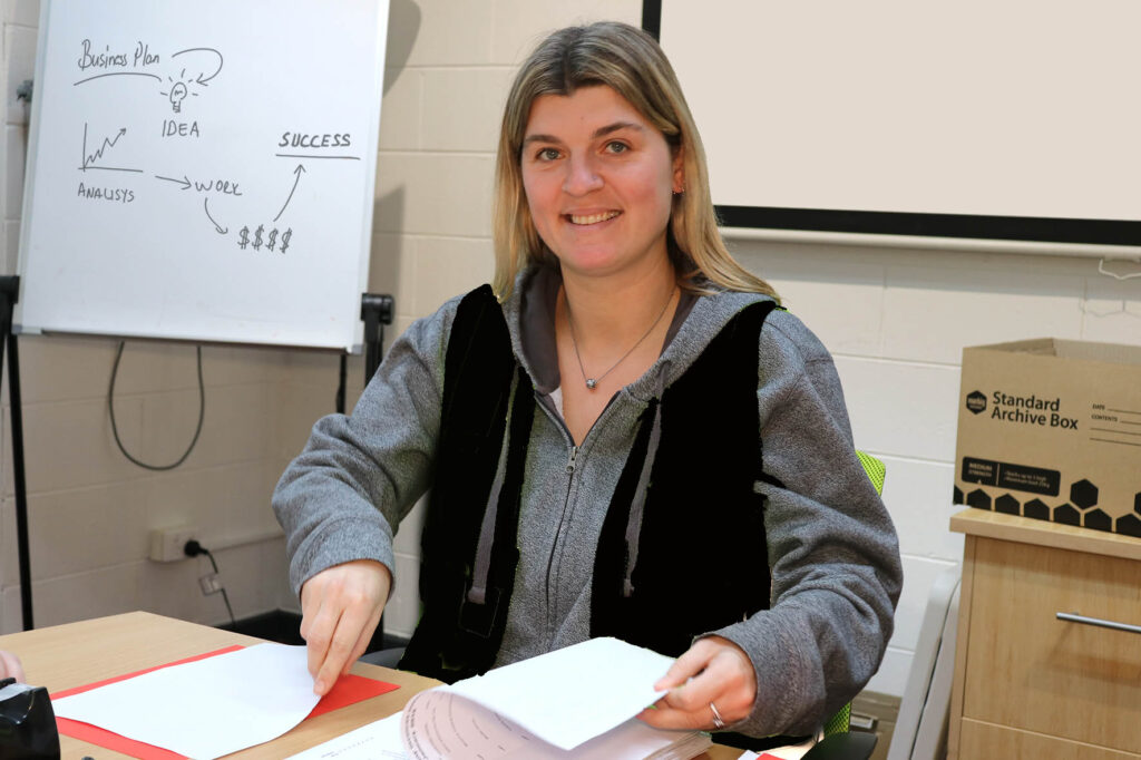 Person sits at a desk and looks at the camera. They are holding paper, ready to file.