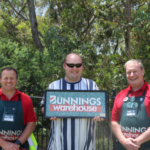 three people standing beside each other. the middle person is holding a mosaic sign that reads Bunnings warehouse