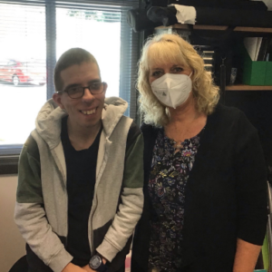 Two people standing together. One is wearing glasses. The other wearing a face mask
