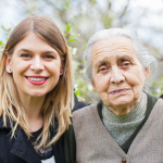 A young woman stands close to an elderly lady. both look into the camera
