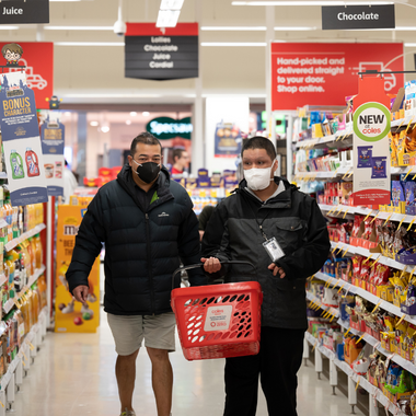 Two people in a supermarket aisle, with masks on. One is holding a basket.
