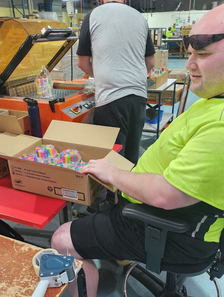 Supported employee Peter, sits at table and packs Crayola crayons into boxes at OCCE